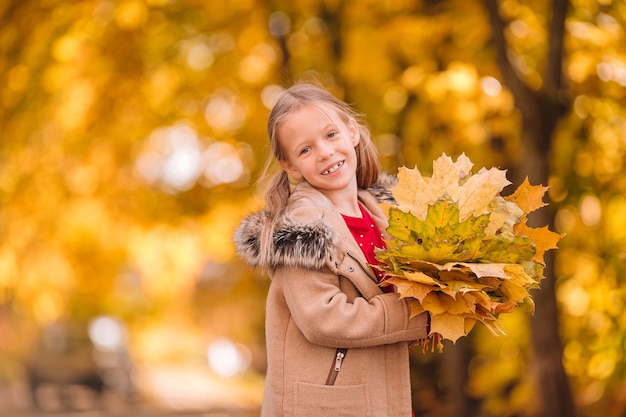 Retrato de niña adorable con ramo de hojas amarillas en otoño