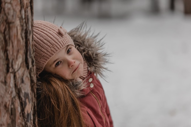 Retrato de niña adorable en sombrero de invierno en bosque nevado