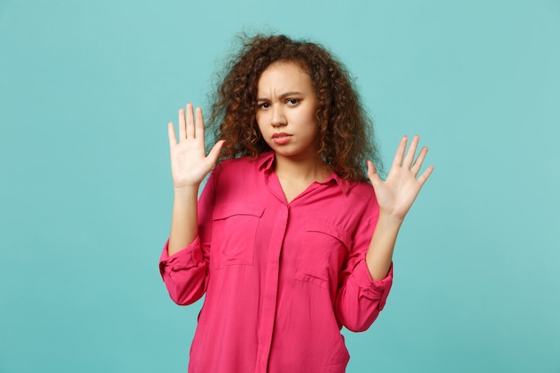 Retrato de niña africana preocupada en ropa casual levantando las manos, mostrando la palma aislada sobre fondo de pared azul turquesa en estudio. Concepto de estilo de vida de emociones sinceras de personas. Simulacros de espacio de copia.