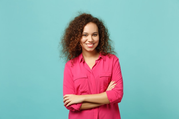 Retrato de niña africana sonriente en ropa casual rosa cogidos de la mano cruzados aislados sobre fondo de pared azul turquesa en estudio. Personas sinceras emociones, concepto de estilo de vida. Simulacros de espacio de copia.