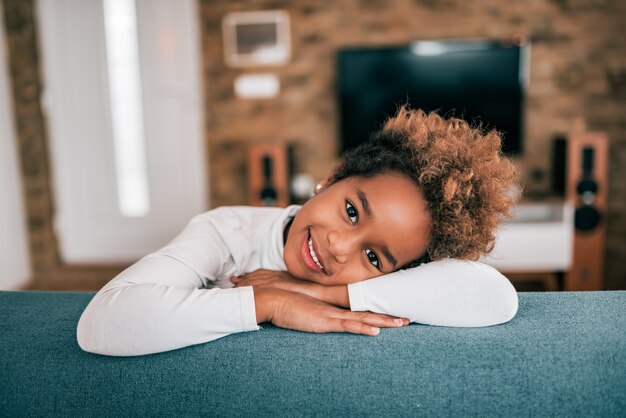 Retrato de una niña afroamericana feliz en el sofá, mirando a la cámara.