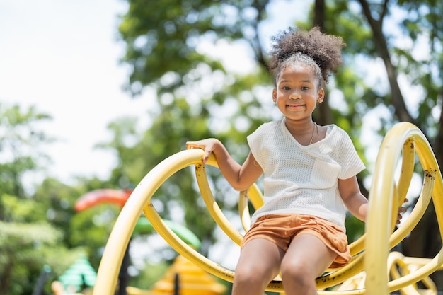 Retrato de una niña afroamericana feliz sonriendo mirando a la cámara en el patio de recreo en el parque