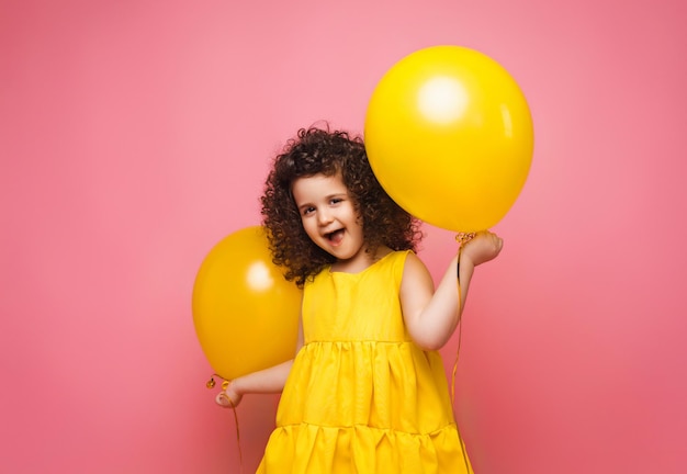 Retrato de una niña alegre aislada en un fondo rosa sosteniendo un montón de globos coloridos posando