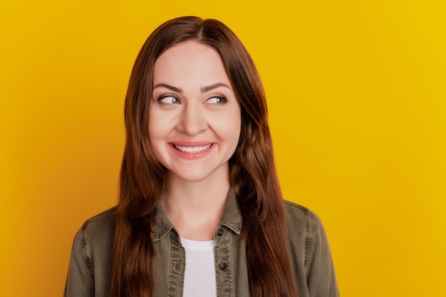 Retrato de niña alegre inspirada soñadora sonrisa con dientes mirar espacio vacío lateral sobre fondo amarillo