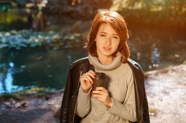 Retrato de una niña alegre en la naturaleza con una copa de café