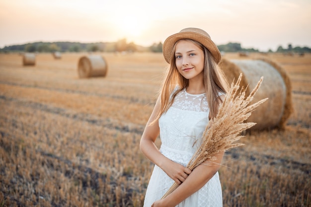 Retrato de una niña alegre con un ramo de flores de otoño con un vestido blanco claro y un sombrero de paja