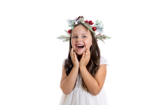 Retrato de niña alegre sorprendida con la boca abierta en corona de navidad disfrutando de las vacaciones de navidad ...