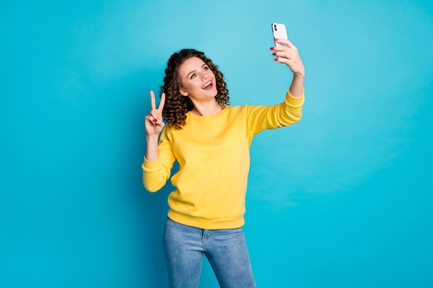 Retrato de niña alegre tomando selfie showi v-sign aislado sobre fondo azul.