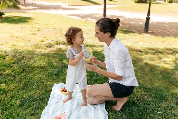 Retrato de una niña alegre en traje de verano con rizos con mamá. ella está jugando con la madre