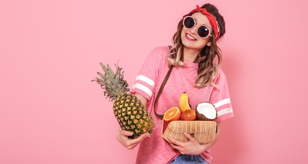 Retrato de una niña con alimentos saludables, frutas, en una pared rosa