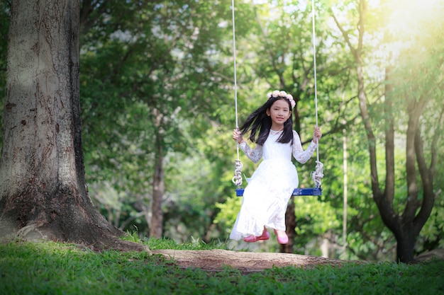 Retrato de niña asiática jugando el columpio bajo el gran árbol en el bosque natural