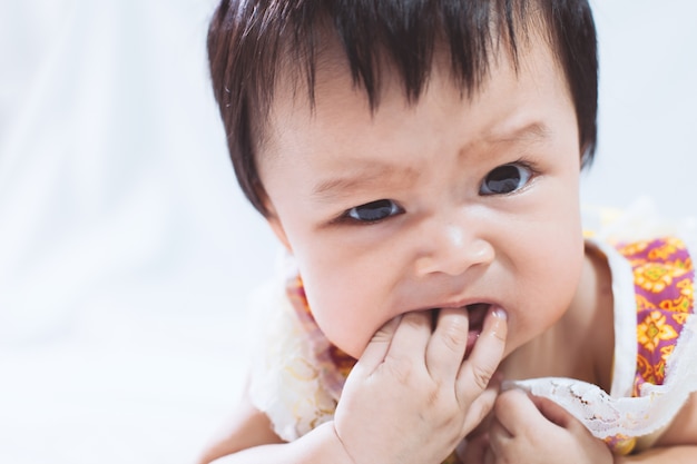 Retrato de niña asiática linda chupando los dedos en la boca sobre fondo blanco