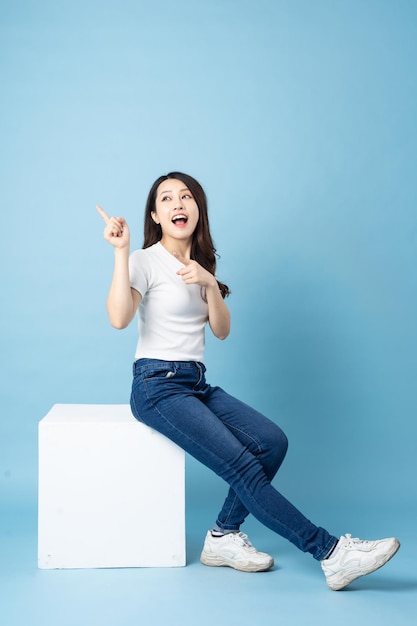 Retrato de niña asiática sentada en un cubo blanco, aislado sobre fondo azul.