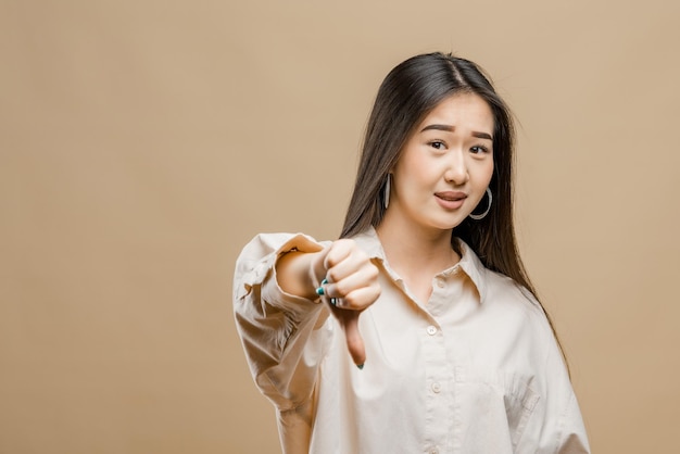 Retrato de una niña asiática sobre un fondo marrón claro niña asiática muestra los pulgares hacia abajo