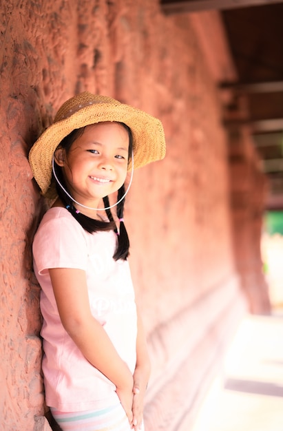 Retrato de niña asiática con sombrero de pie cerca de la pared