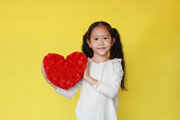 Retrato de niña asiática sonriente sosteniendo un corazón rojo