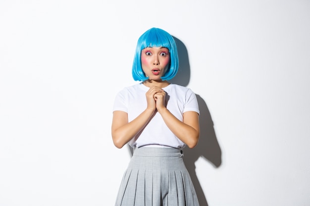 Retrato de niña asiática sorprendida en peluca corta azul jadeando asombrado, escuchar algo impactante, de pie en traje de halloween.