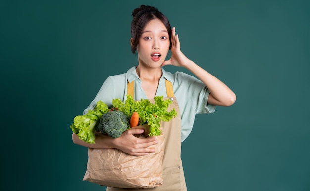 Retrato de niña asiática sosteniendo una bolsa de verduras sobre un fondo verde