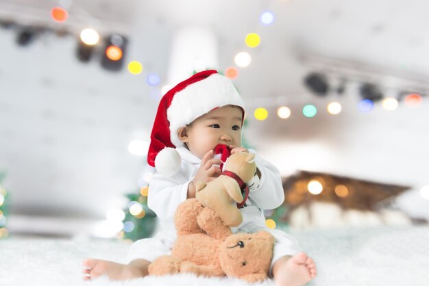 Retrato de niña asiática usar sombrero de santa con oso dollThailand personas en el fondo del árbol de Navidad