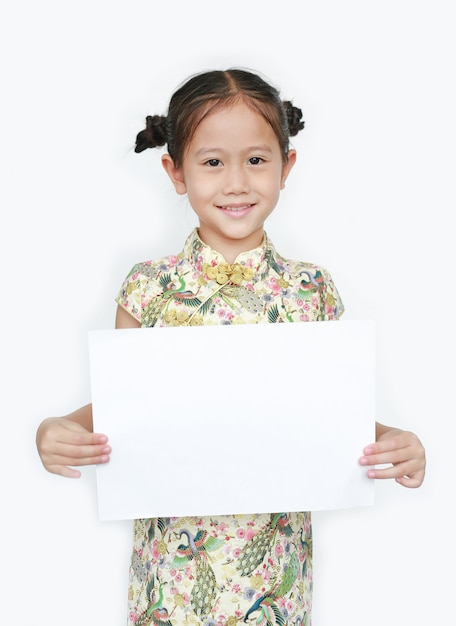 Retrato de niña asiática vistiendo cheongsam con sonriente y sosteniendo papel blanco en blanco aislado