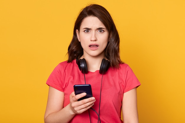 Retrato de niña asombrada usa el teléfono celular para leer notificaciones de redes sociales, queda impresionada y conmocionada