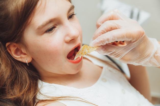 Retrato de una niña con la boca abierta sentada en la silla de un dentista mientras un ortodoncista sostiene un plato en sus dientes El dentista pone un plato en la boca de un niño