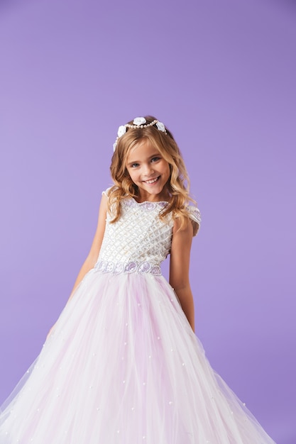 Retrato de una niña bonita alegre sonriente vestida con un vestido de princesa aislado sobre la pared violeta, bailando