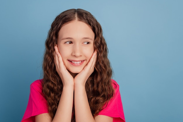 Retrato de niña bonita y atractiva soñadora manos pómulos sonrisa blanca dentuda mirar espacio en blanco sobre fondo azul.