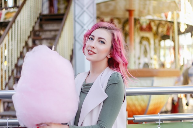 Retrato de niña bonita con cabello rosado con corte de pelo corto posando en el parque de atracciones en el fondo del carrusel. mujer con cabello rosado ombre con lentejuelas fotodiñendo rizos de cabello moda brillo brillante