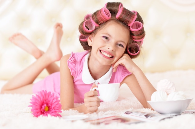 Foto retrato de niña bonita feliz en rizadores de pelo con té