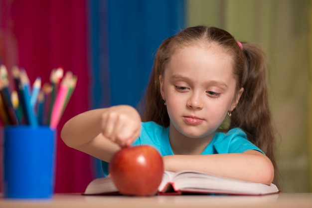 Retrato de niña bonita feliz sosteniendo una manzana roja en el aula