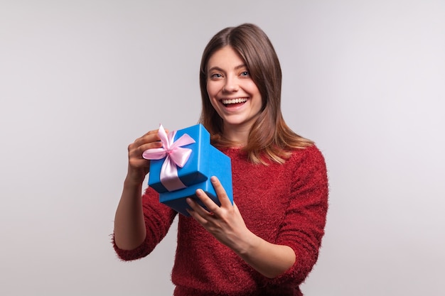 Foto retrato de niña bonita feliz en suéter abriendo caja de regalo y mirando a cámara satisfecho sonriendo