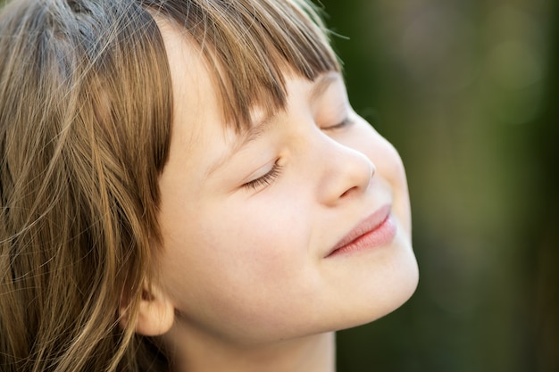 Retrato de niña bonita joven con el pelo largo disfrutando de cálido día soleado en verano al aire libre. Lindo niño femenino relajante en aire fresco afuera.