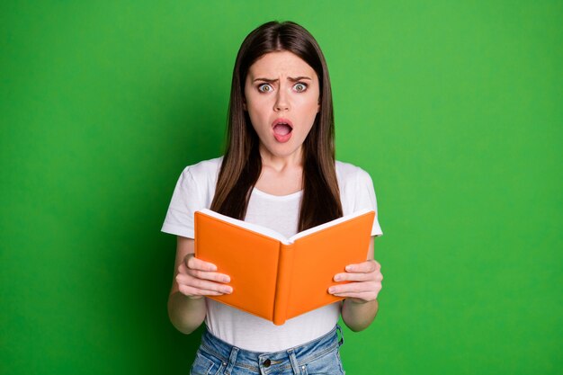 Retrato de niña bonita morena impresionada mantenga libro use camiseta blanca aislada sobre fondo de color verde