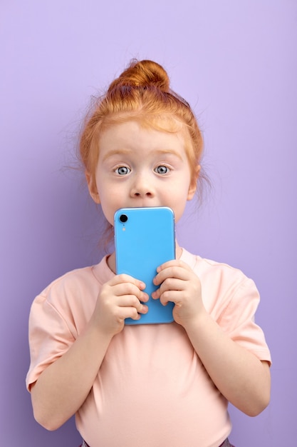 Retrato de niña bonita pelirroja con smartphone aislado en púrpura