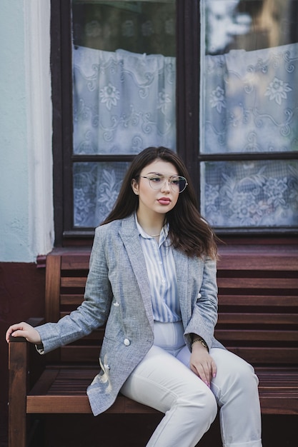 Retrato de niña bonita con pelo largo y rizado sentado en la ciudad. Lleva chaqueta elegante.