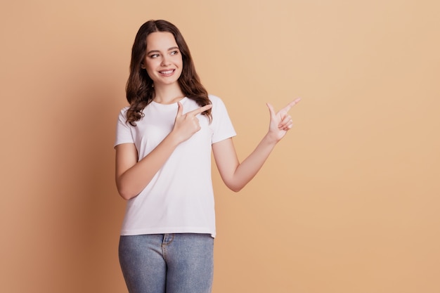 Retrato de niña bonita positiva indican los dedos espacio vacío aislado sobre fondo beige