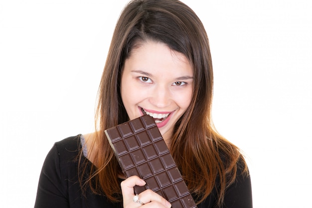 Retrato de una niña bonita satisfecha mordiendo barra de chocolate sonriendo