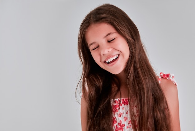 Retrato de una niña bonita sobre un fondo gris, cerró los ojos de placer y sonríe.