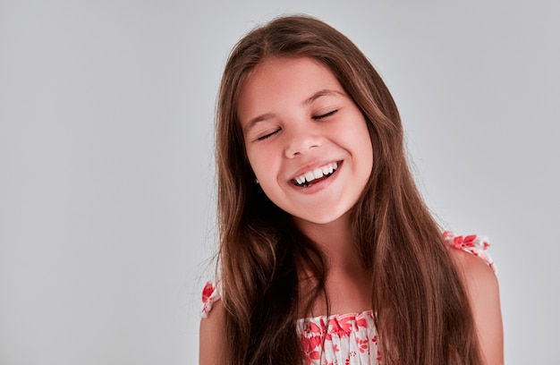 Retrato de una niña bonita sobre un fondo gris, cerró los ojos de placer y sonríe.