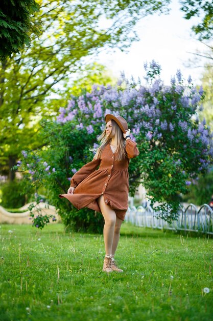 Retrato de una niña bonita con un sombrero marrón con una lila en el jardín