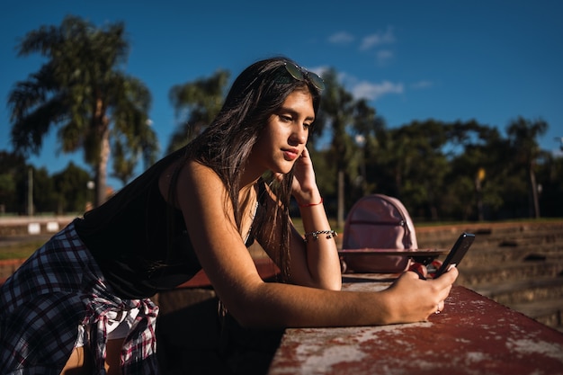 Retrato de una niña bonita con su smartphone en un parque urbano.