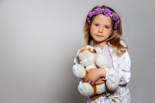 Foto retrato de niña bonita en vestido blanco y corona de color púrpura con peluche tigre