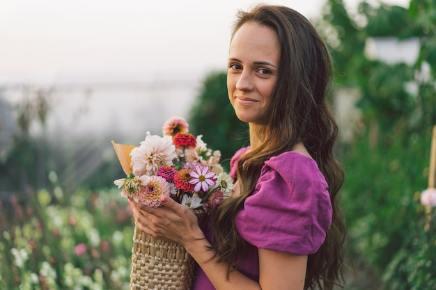 Retrato de niña con cabello largo con una canasta de flores. Camina por el jardín de flores. Niña y flores. Florística.