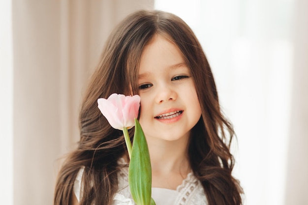 Retrato de una niña con cabello largo y oscuro primer plano El bebé abraza un ramo de tulipanes rosas frescos y delicados Un regalo para las vacaciones de primavera