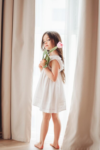 Retrato de una niña con cabello largo y oscuro primer plano El bebé abraza un ramo de tulipanes rosas frescos y delicados Un regalo para las vacaciones de primavera