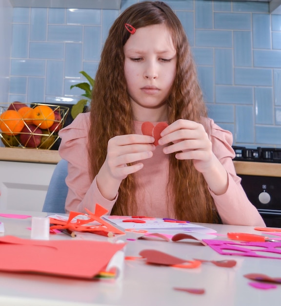 Retrato de una niña con cabello largo y oscuro sosteniendo un corazón rojo cortado de papel Día de San Valentín