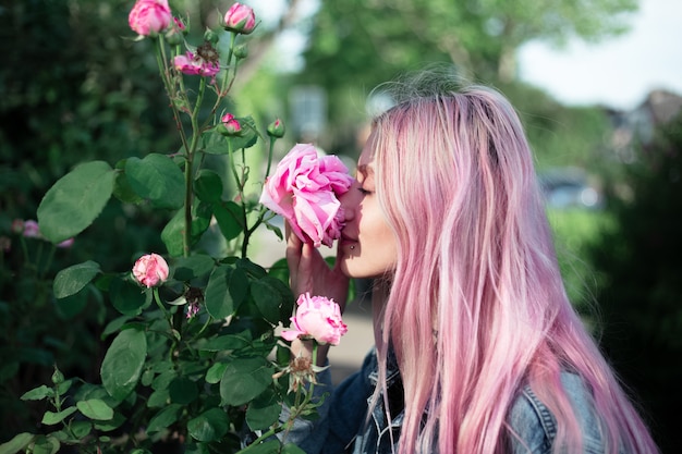 Retrato de niña con cabello rosado oliendo flor color de rosa.