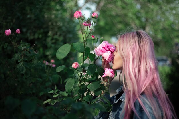 Retrato de niña con cabello rosado oliendo flor color de rosa.