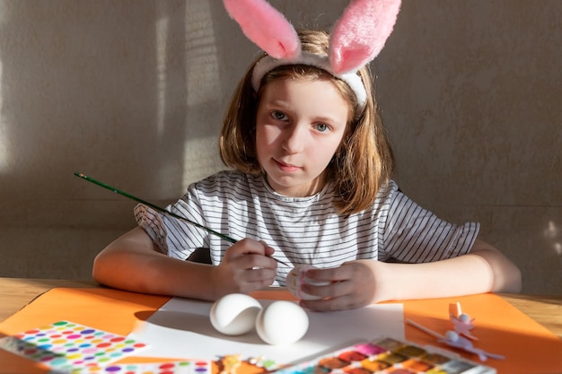 Retrato de niña caucásica decorando huevos de pascua en la cocina doméstica vacaciones familia y concepto de personas niña con orejas de conejo haciendo decoración de Pascua